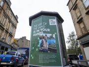 The Land of the Land is in Your Hands poster in place with traditional sandstone tenement buildings