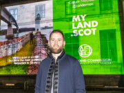 Calum Maclean, host of the MyLand.scot 'Lay of the Land' podcast, poses in front of his film projected onto the Scottish National Gallery of Modern Art building. Credit: Adam Kenrick.
